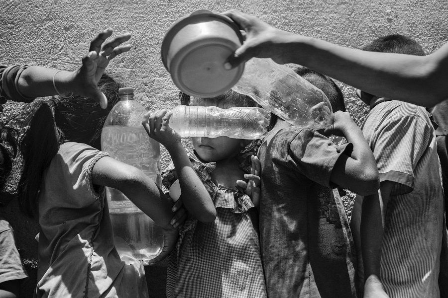 Venezuelan children holding plastic bottles to be filled with water wait in line for a free meal at a charity organization in Paraguachón, Colombia.